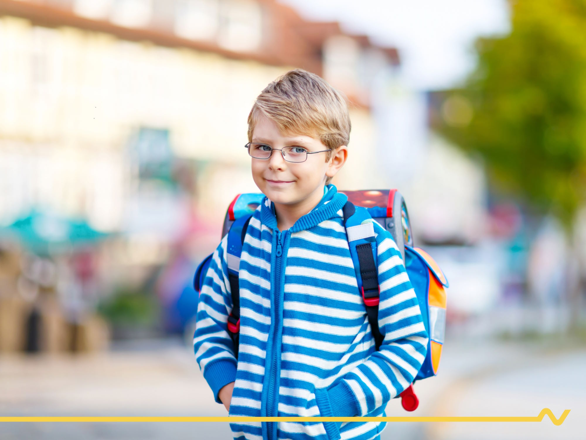 Vor der Volksschule: Schulbub mit blau-weiß-gestreiftem Pullover und Schultasche blickt in Richtung Kamera.